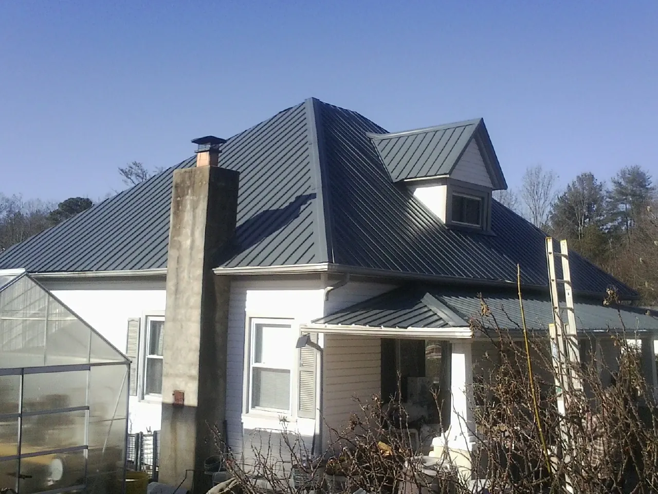 Dark blue standing seam metal roof on a white farmhouse with dormer — Slate & Tile Roof Repair by Roofing Brothers in Holly Springs