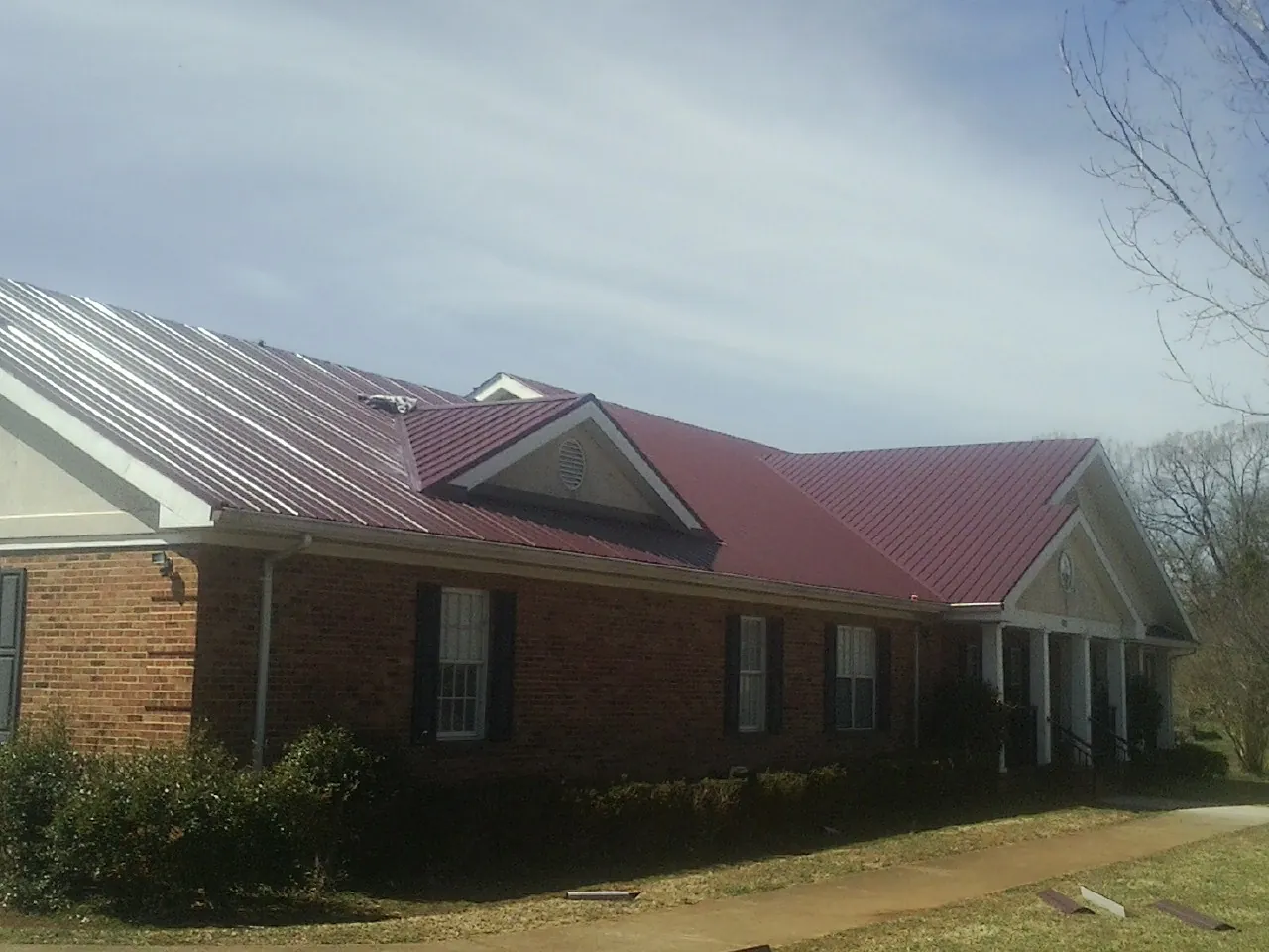 Red metal roof with gabled entries on a long brick building, from a Hail Damage Roof Repair job in Holly Springs