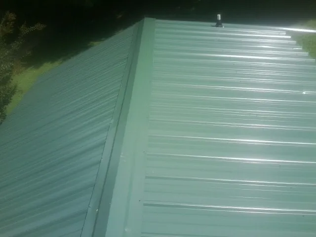 New green metal panels meeting at the ridge of a roof — Flat Roof Repair work by our crew in Holly Springs