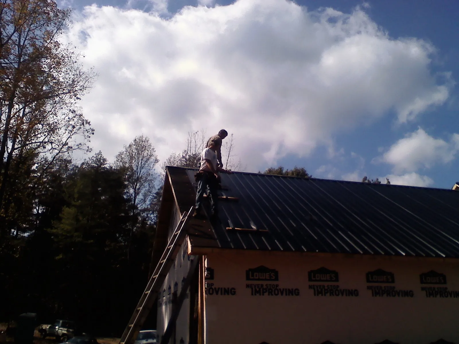 Roofer fastening dark metal panels high against a cloudy sky, from a Roof Inspection job in Holly Springs