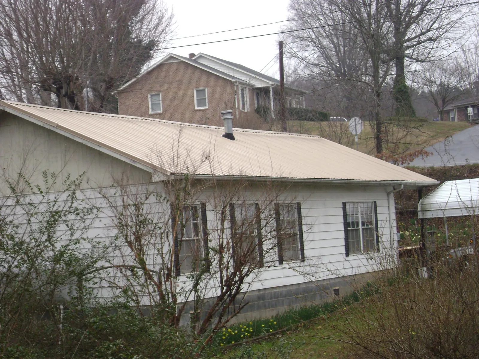 Tan metal roof on a white sided house set into a hillside — Commercial Roofing by Roofing Brothers in Holly Springs
