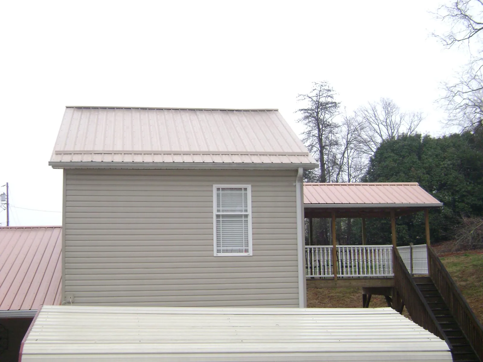 Tan metal roofs on a two story addition and attached porch, from a Roof Replacement job in Holly Springs