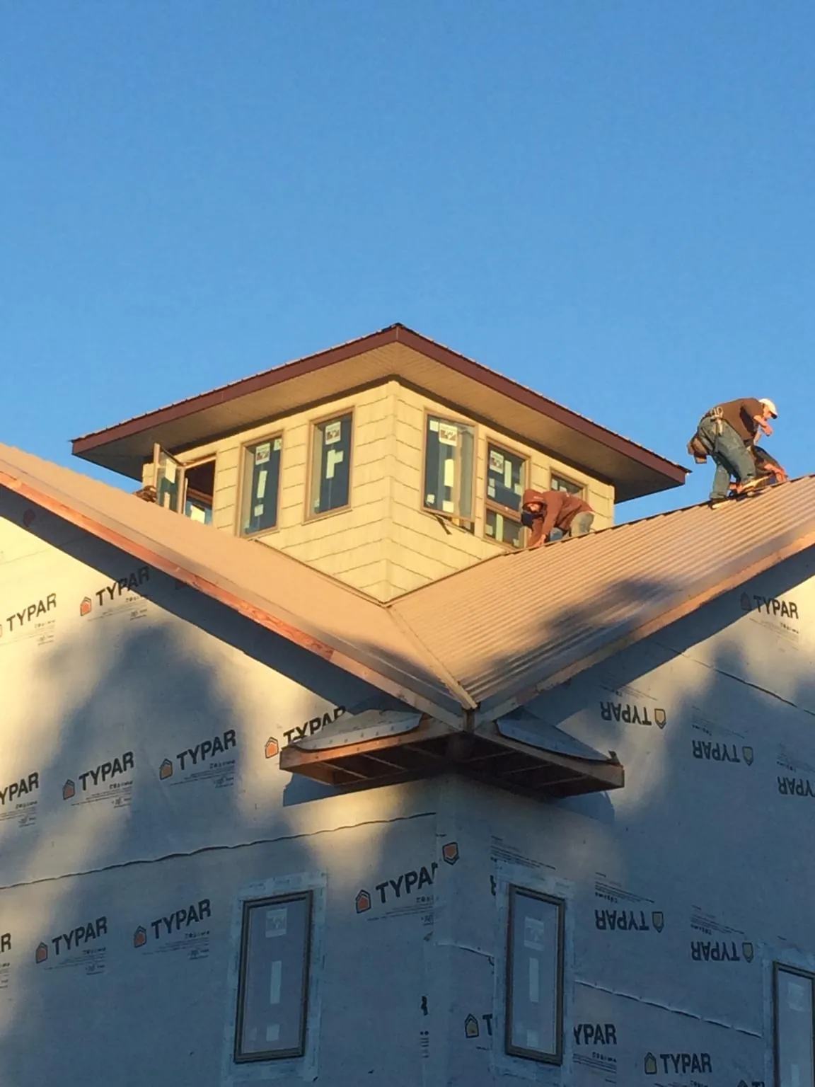 Roofers working around a rooftop cupola on a new metal roof at sunset — Roof Waterproofing in Holly Springs by Roofing Brothers
